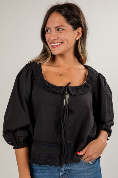 Woman wearing a black blouse with ruffled collar and cuffs against a plain background
