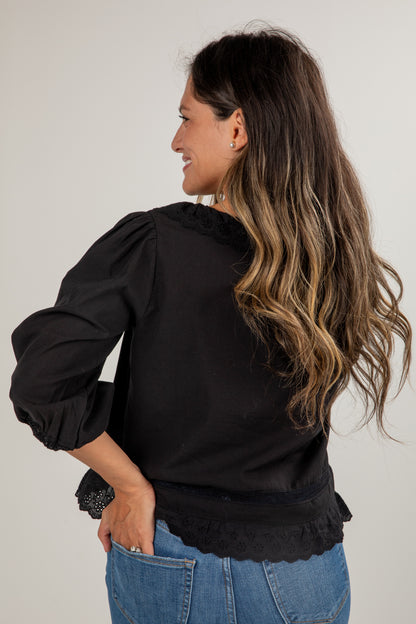 Woman wearing a black blouse with ruffled details and blue jeans on a plain background