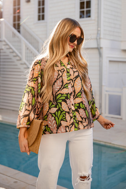 Woman wearing a patterned top and white pants by a poolside.