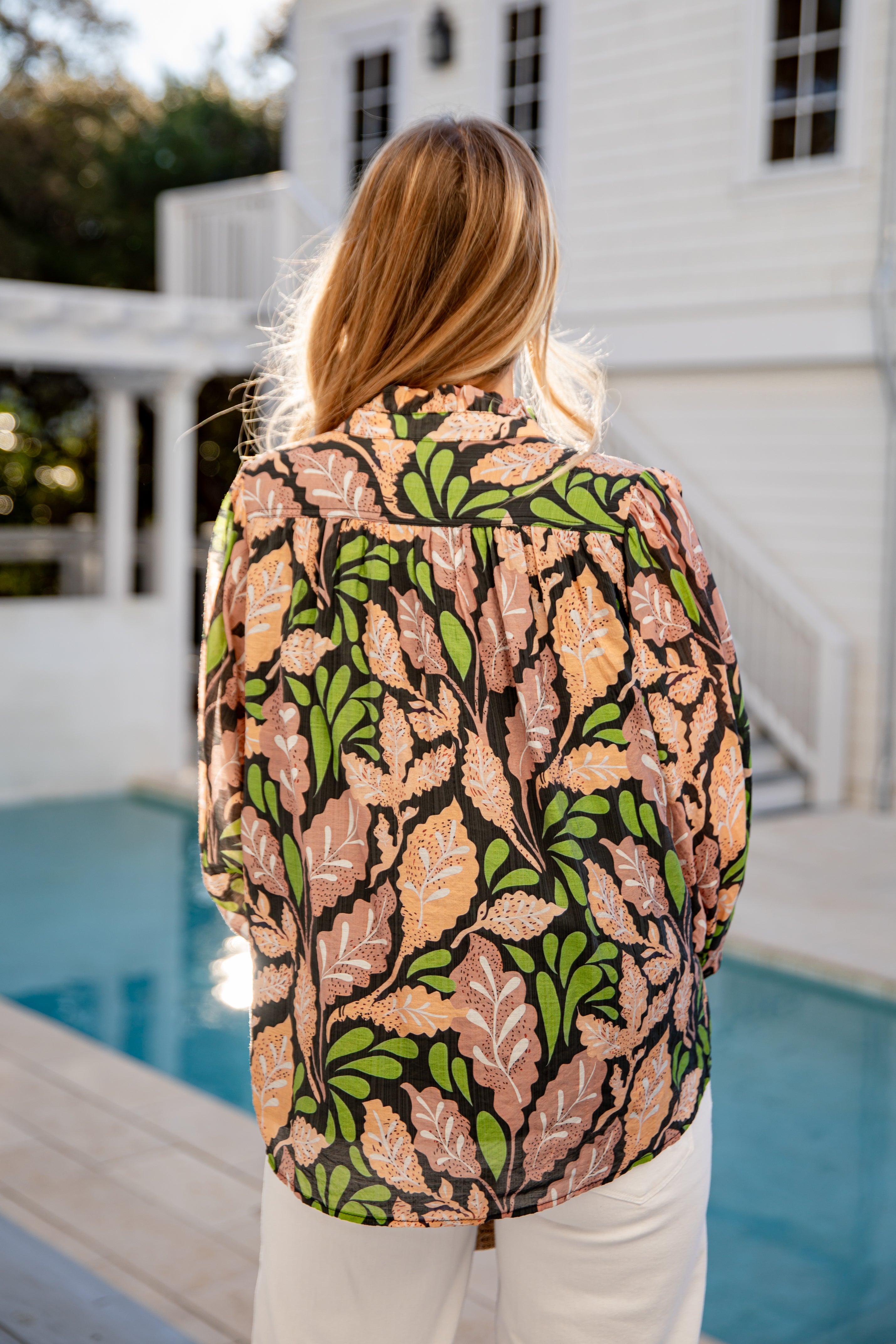 Person wearing a patterned jacket by a poolside with a white building in the background