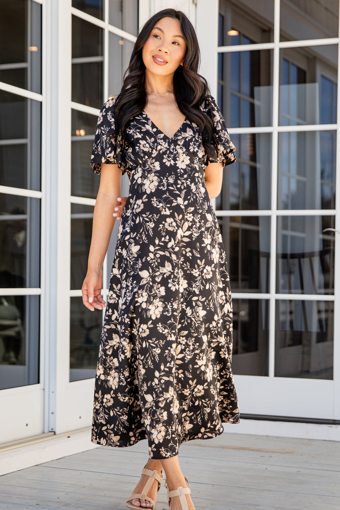 Woman wearing a floral dress standing in front of glass doors.