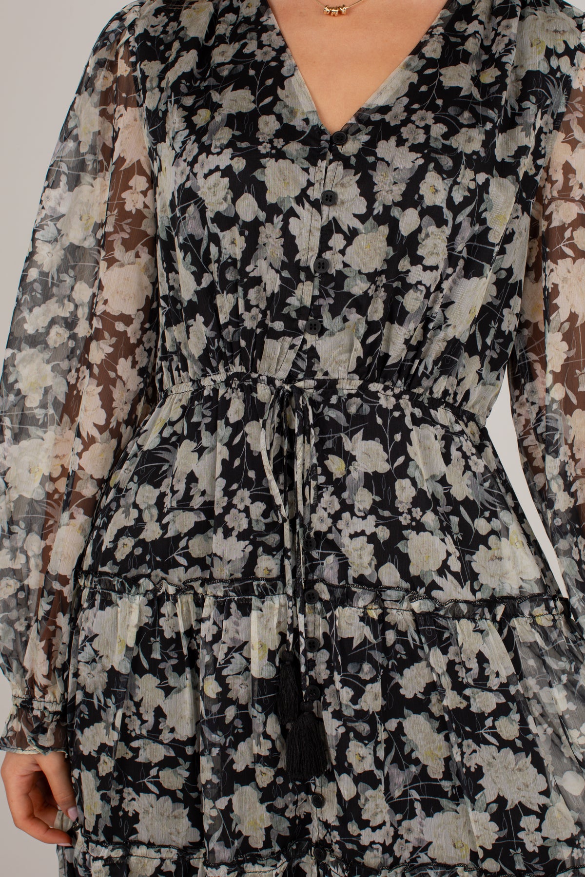 A close-up of a woman wearing a long-sleeve V-neck dress with a black, beige, and gray floral pattern and a matching waist tie.