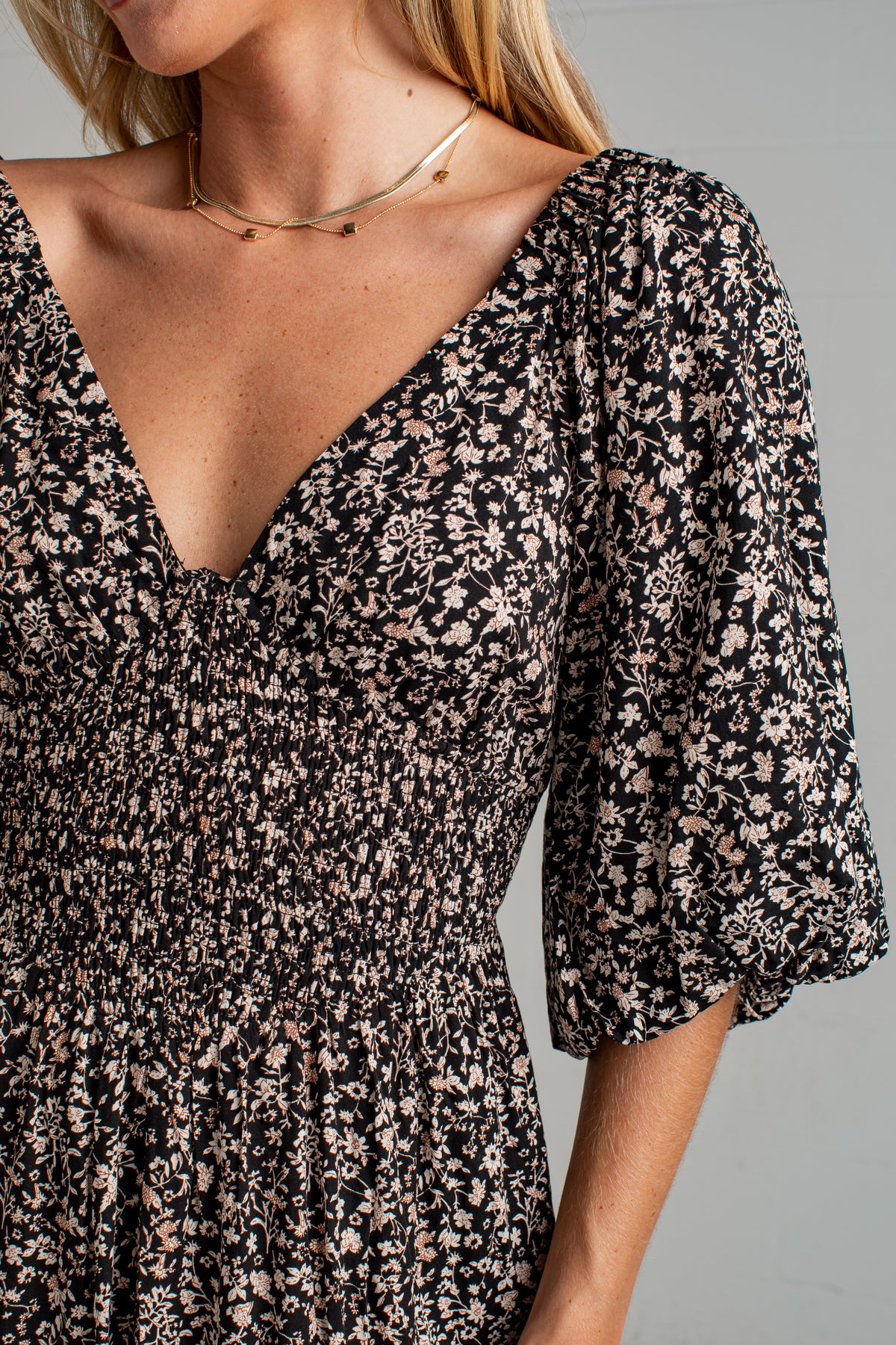Close-up of a woman wearing a black smocked dress with a beige and pink floral print, featuring puff sleeves and a deep V-neckline.