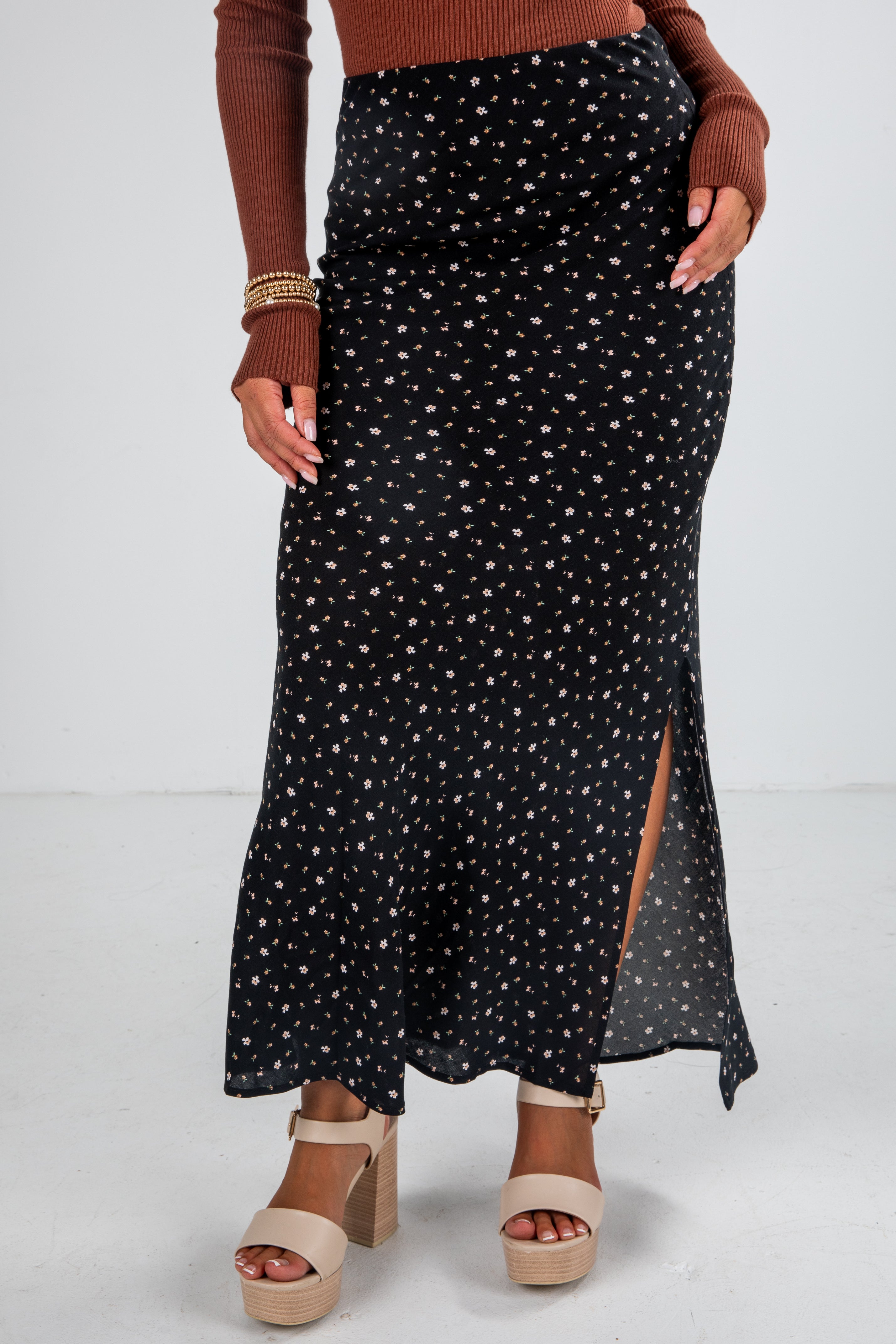 Person wearing a black patterned skirt with a brown top and sandals on a white background