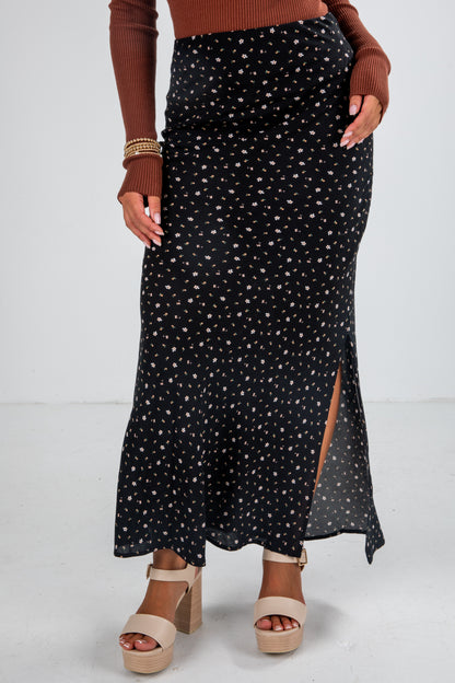 Person wearing a black patterned skirt with a brown top and sandals on a white background