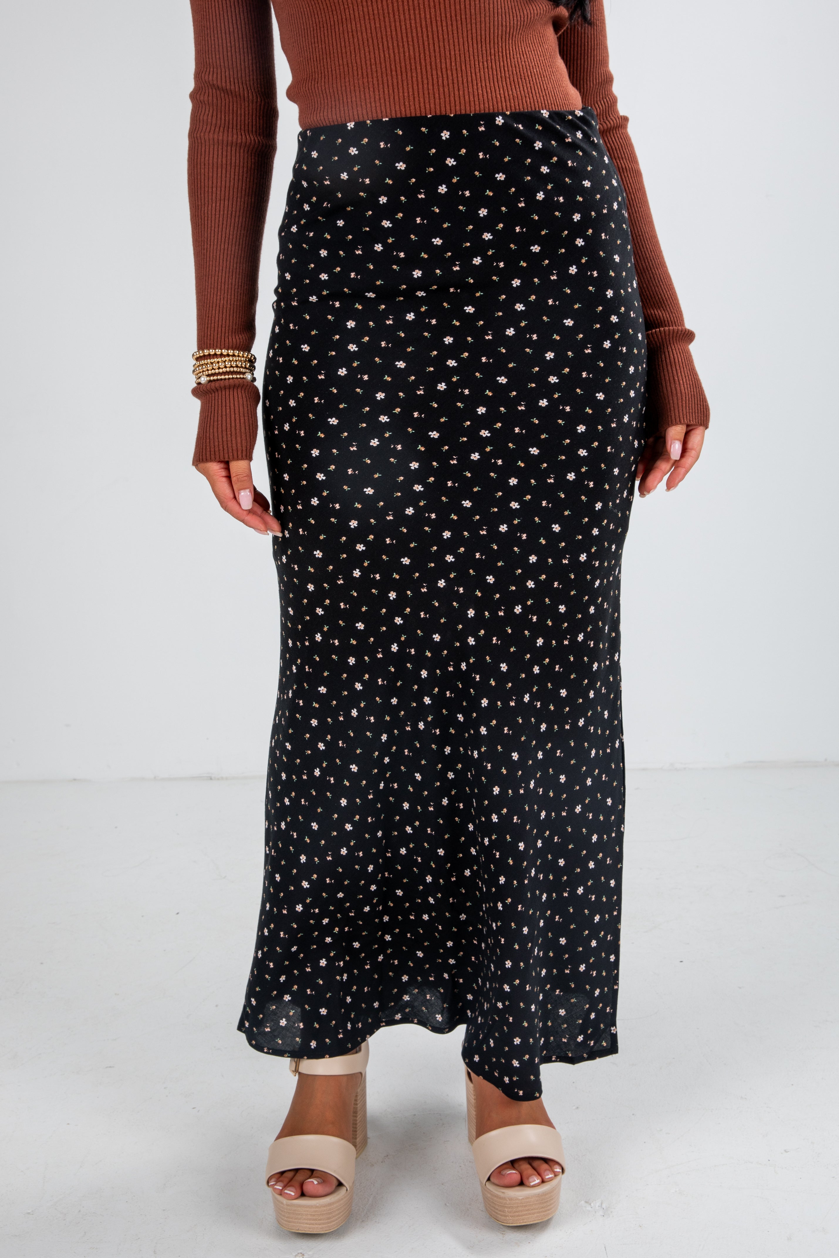 Person wearing a black patterned skirt with a brown top on a white background