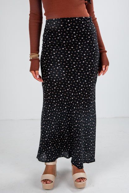 Person wearing a black patterned skirt with a brown top on a white background