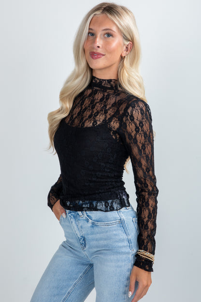 Woman wearing a black lace long-sleeve top and light blue jeans on a white background