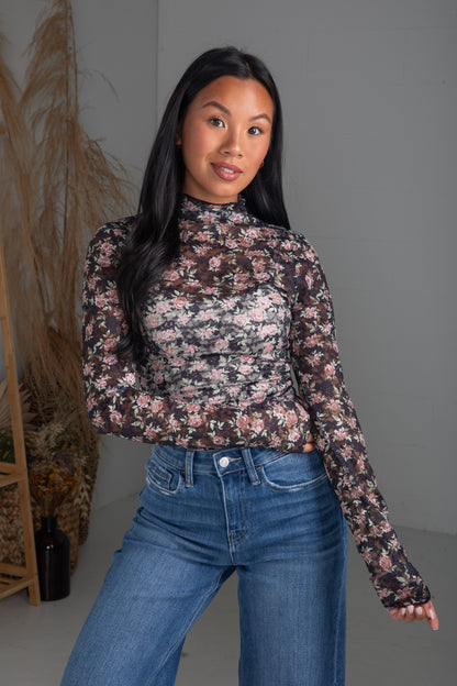 Woman wearing a floral long-sleeve top and blue jeans against a neutral background