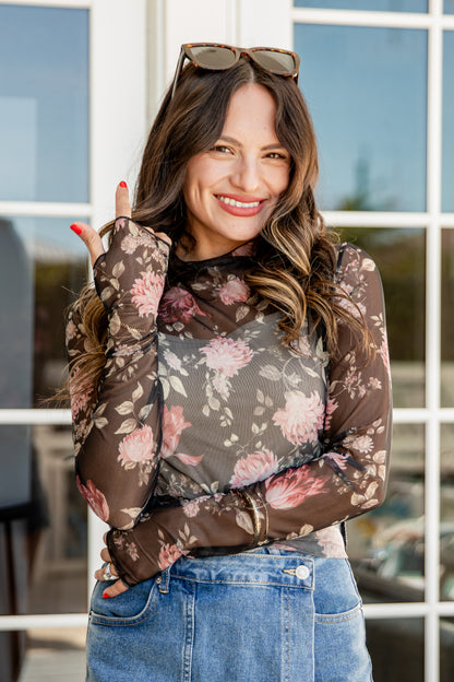 Woman wearing a floral long-sleeve top and jeans outdoors.