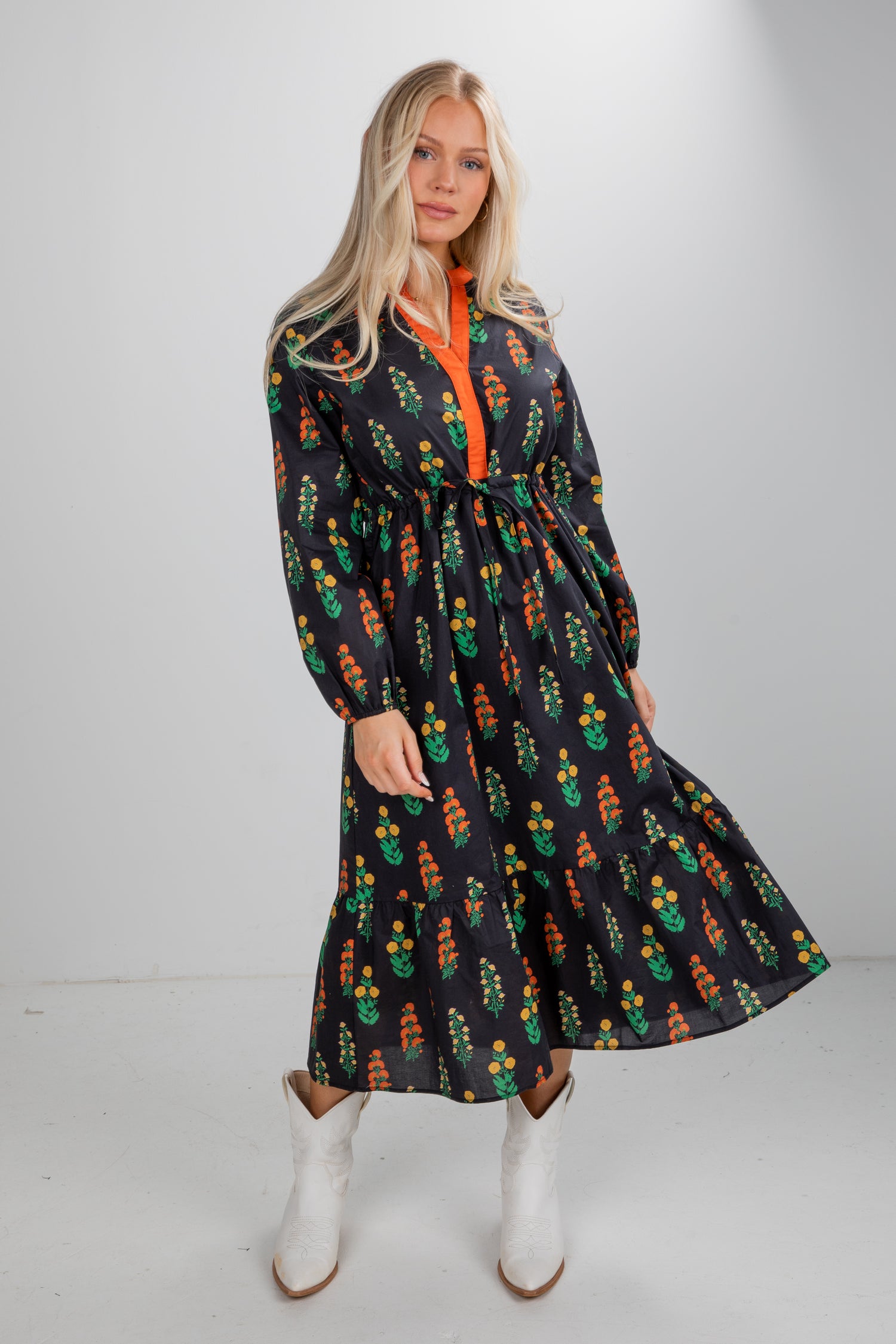 Woman wearing a black dress with colorful patterns and white boots on a plain background