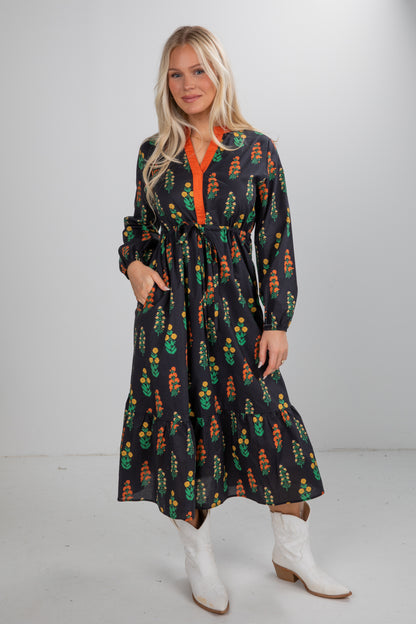 Woman wearing a patterned dress with an orange shirt underneath on a white background