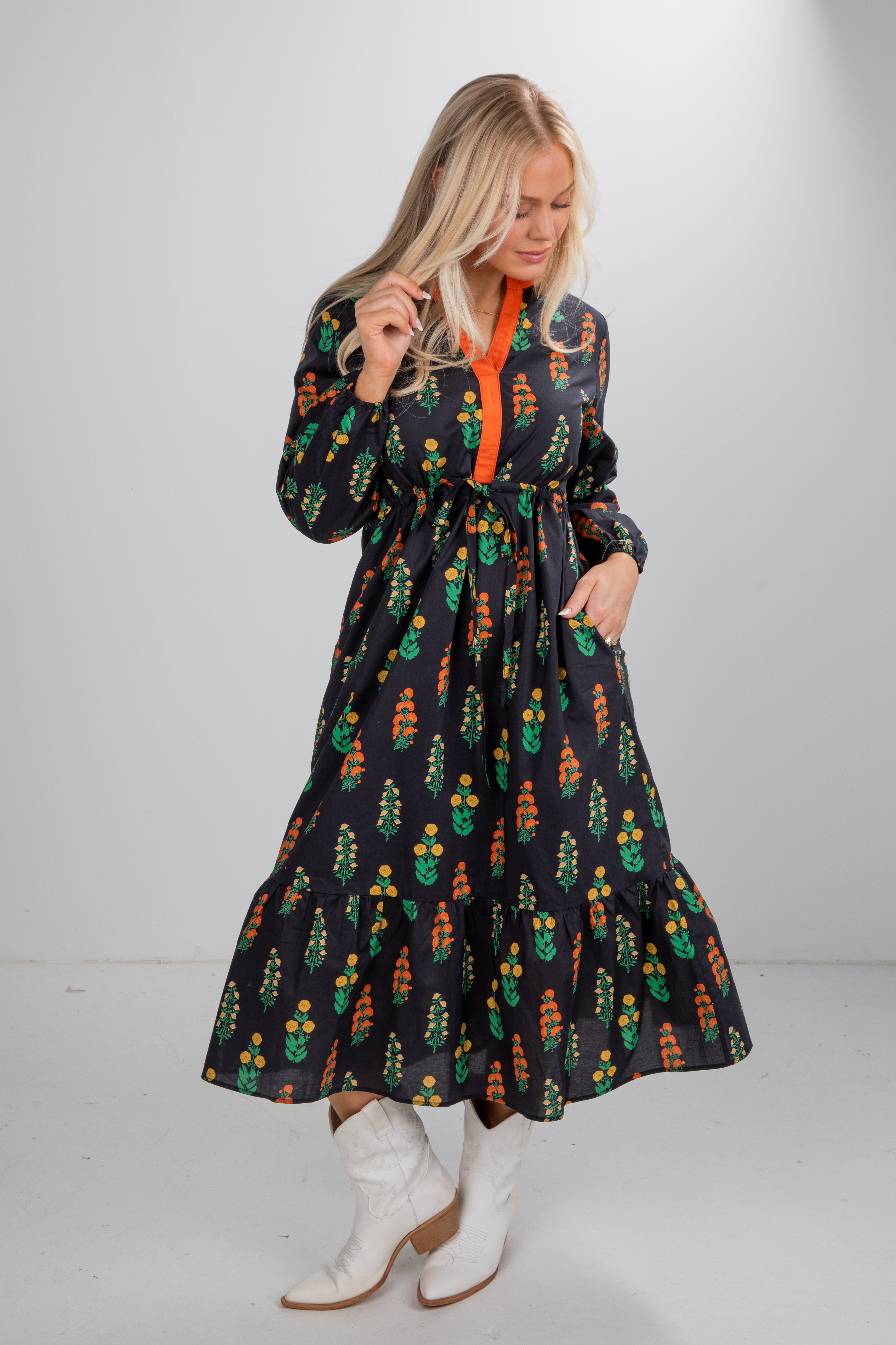 Woman wearing a black dress with colorful cactus pattern and white boots on a plain background