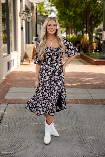 Woman wearing a floral dress and white boots on a city street.