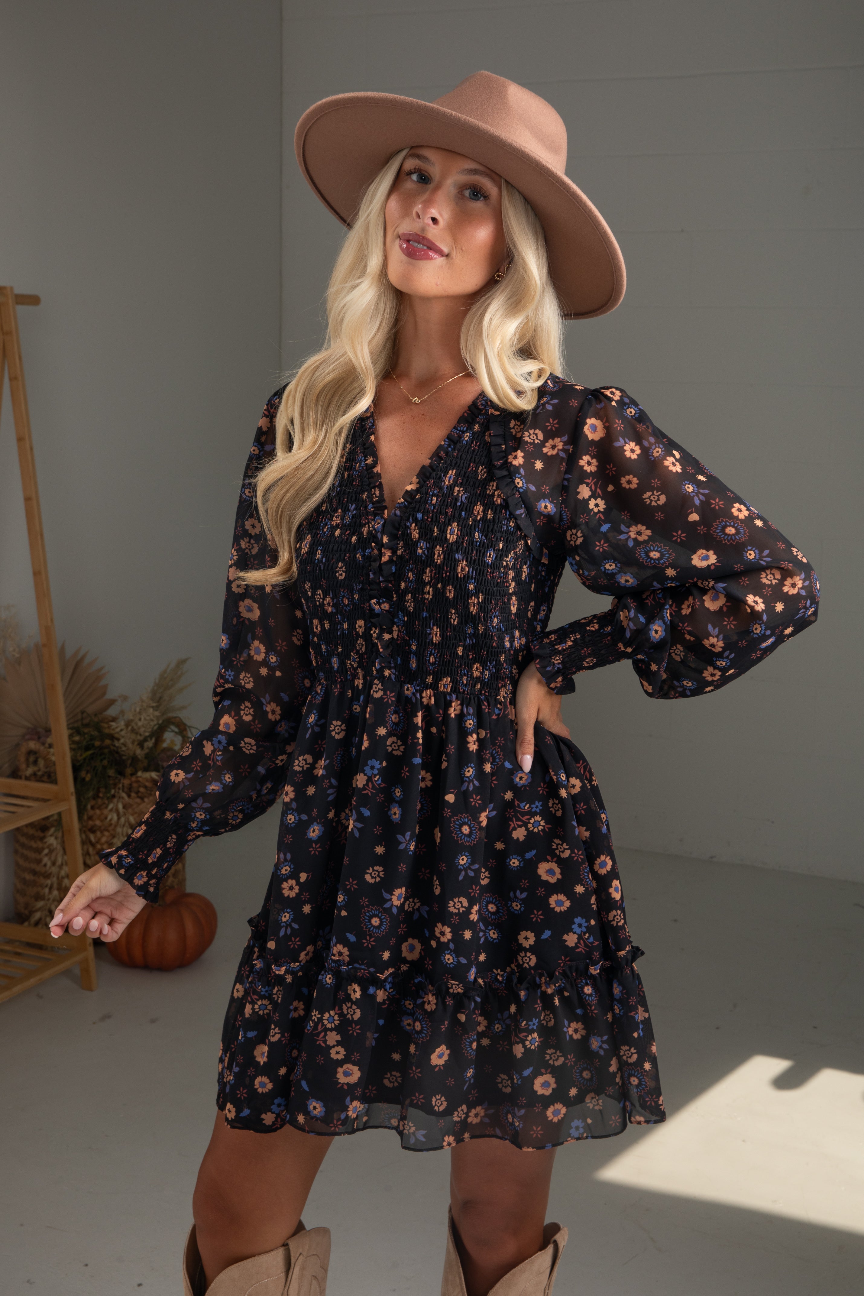 Woman wearing a floral dress and wide-brimmed hat in a neutral setting