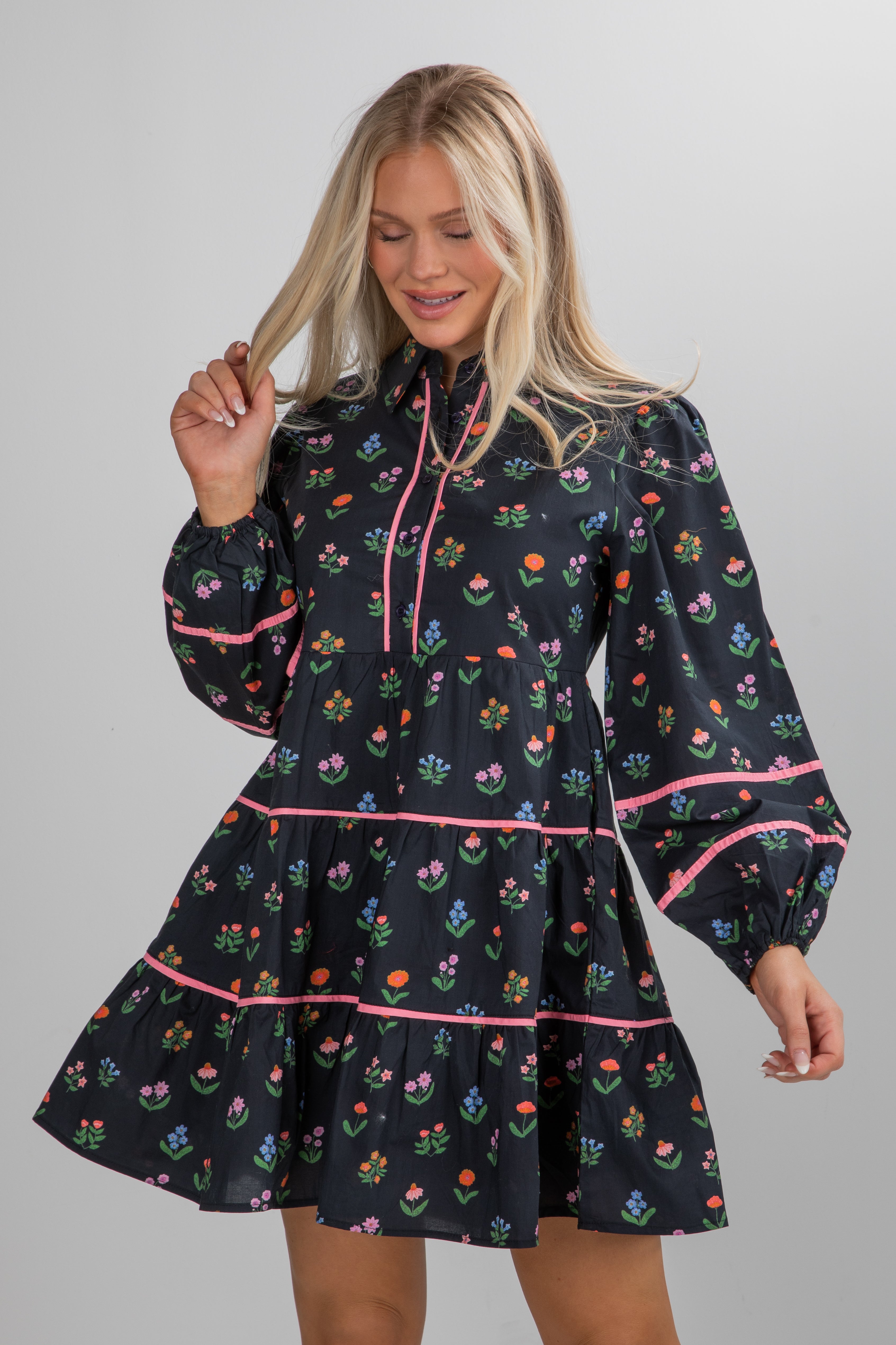 Woman wearing a black dress with floral pattern and pink accents on a gray background