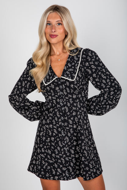 Woman wearing a black floral dress with white trim on a plain background