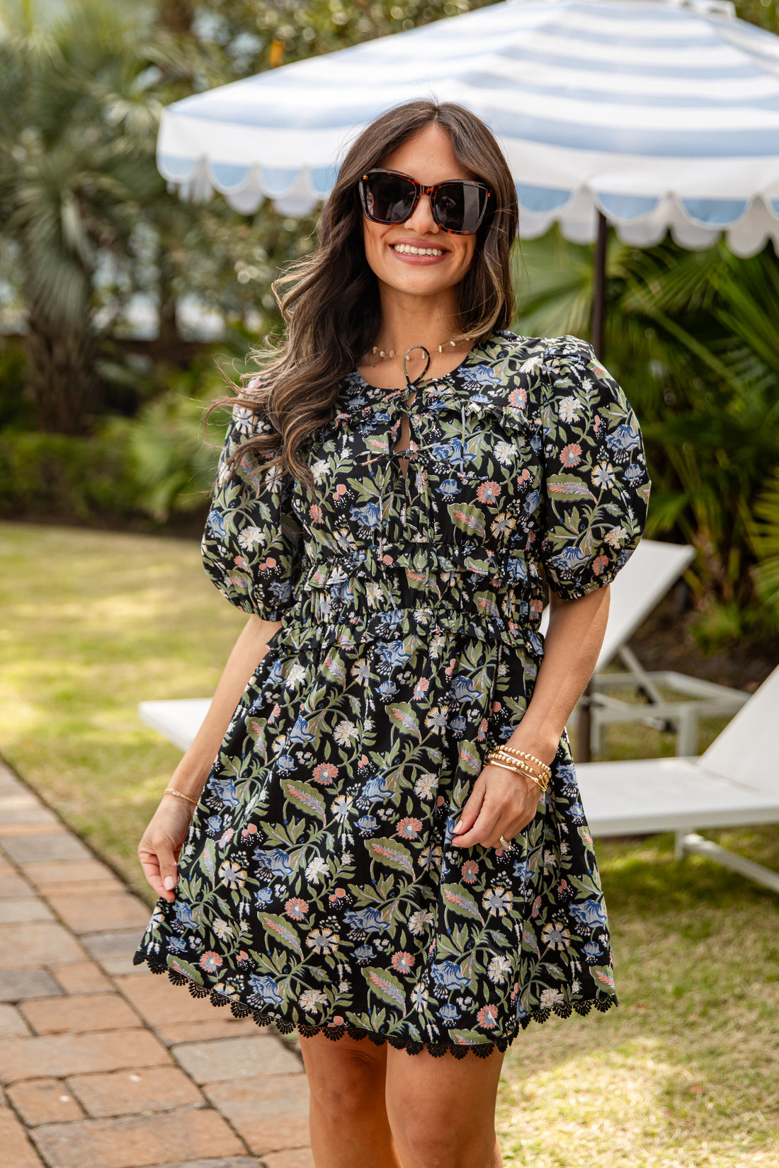 Woman wearing a floral dress standing outdoors under a striped umbrella.