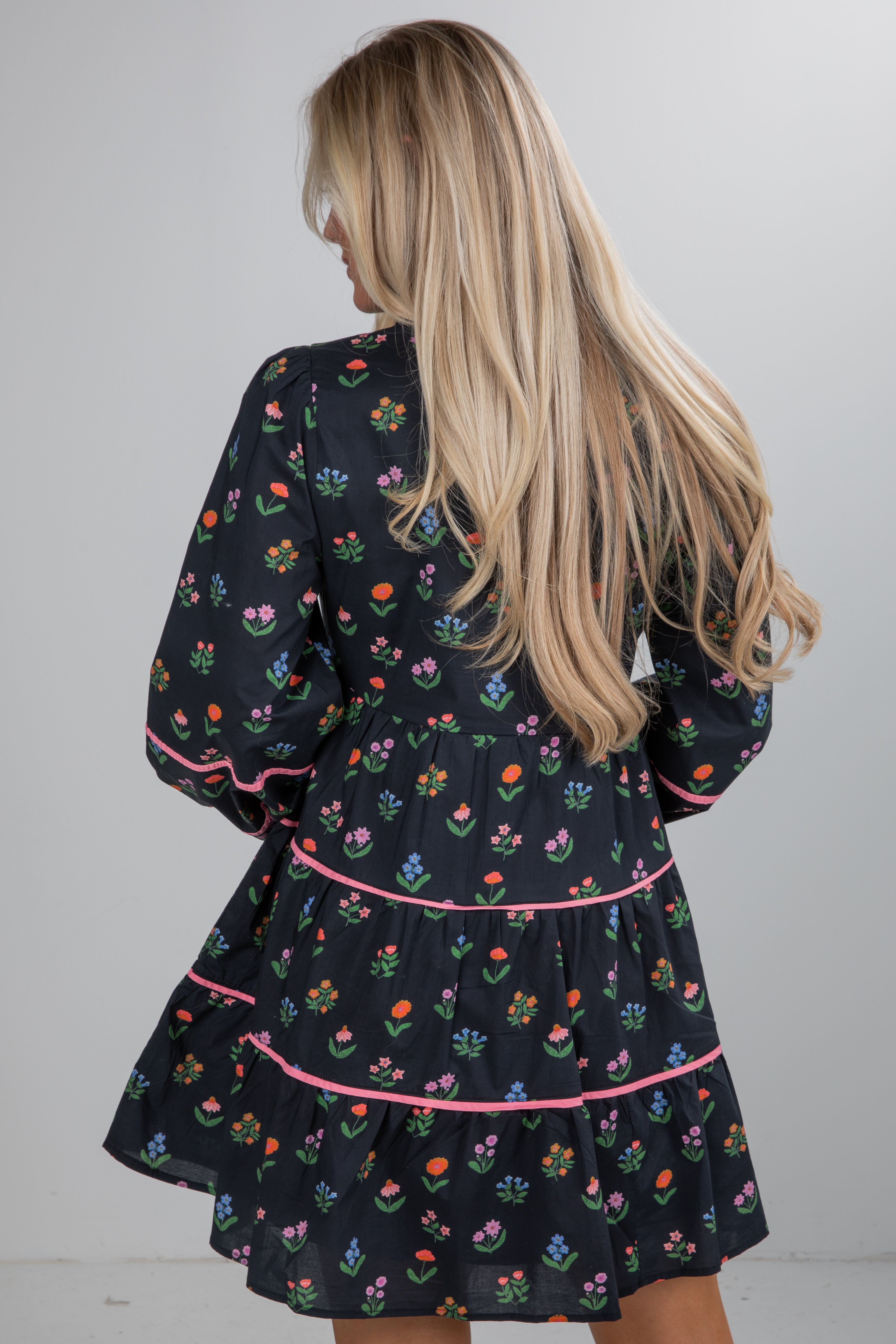 Woman wearing a black dress with colorful floral patterns on a plain background