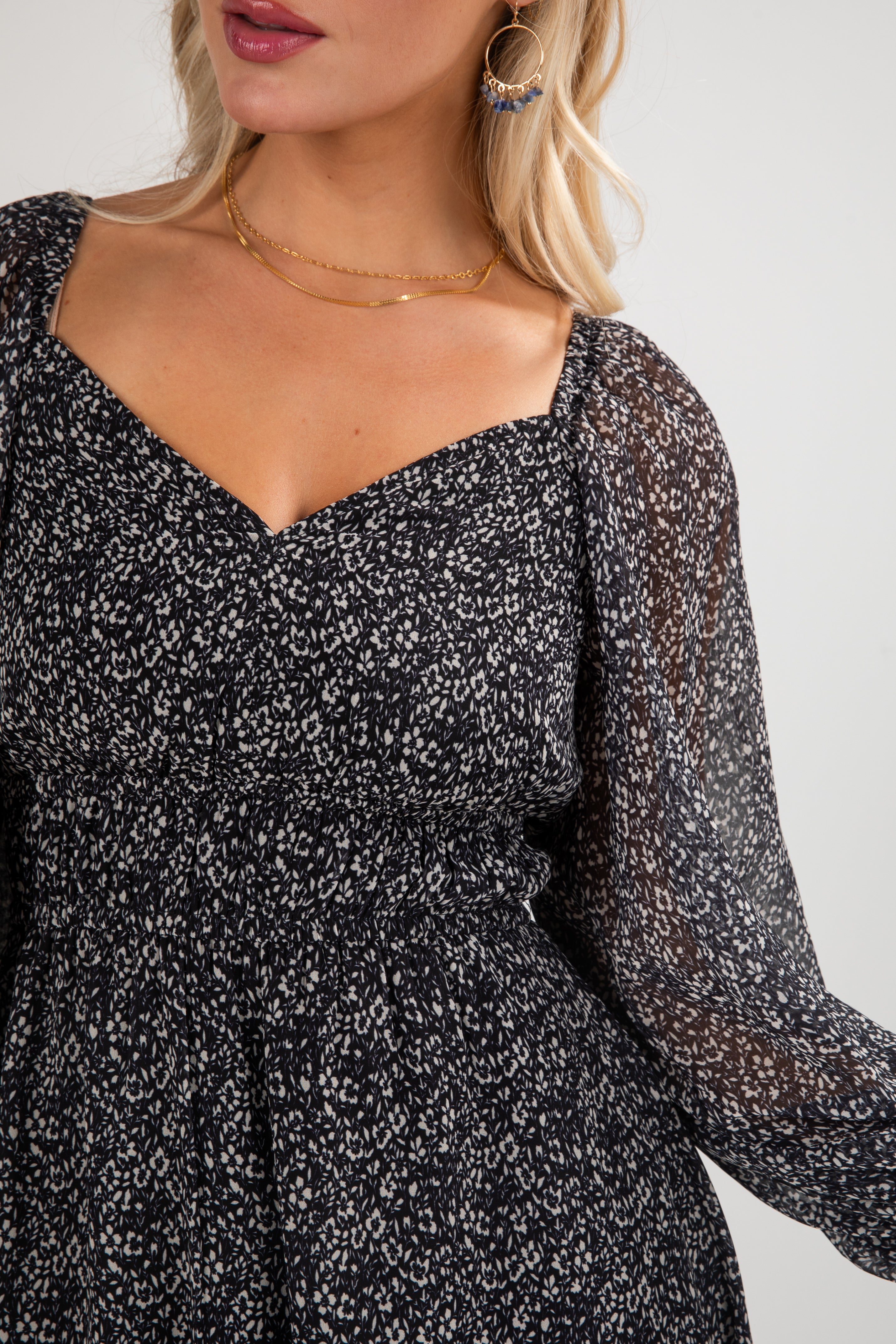 Woman wearing a black floral dress with sheer long sleeves on a white background