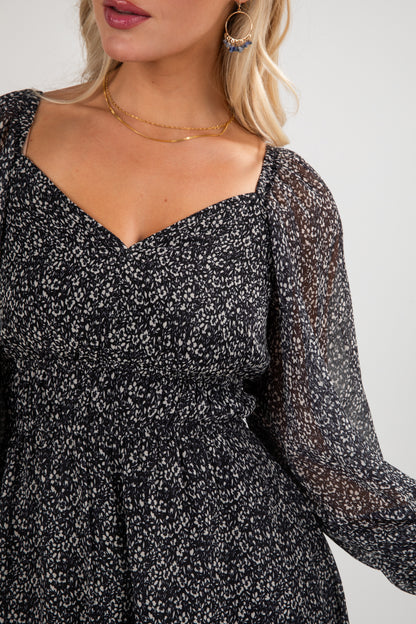 Woman wearing a black floral dress with sheer long sleeves on a white background