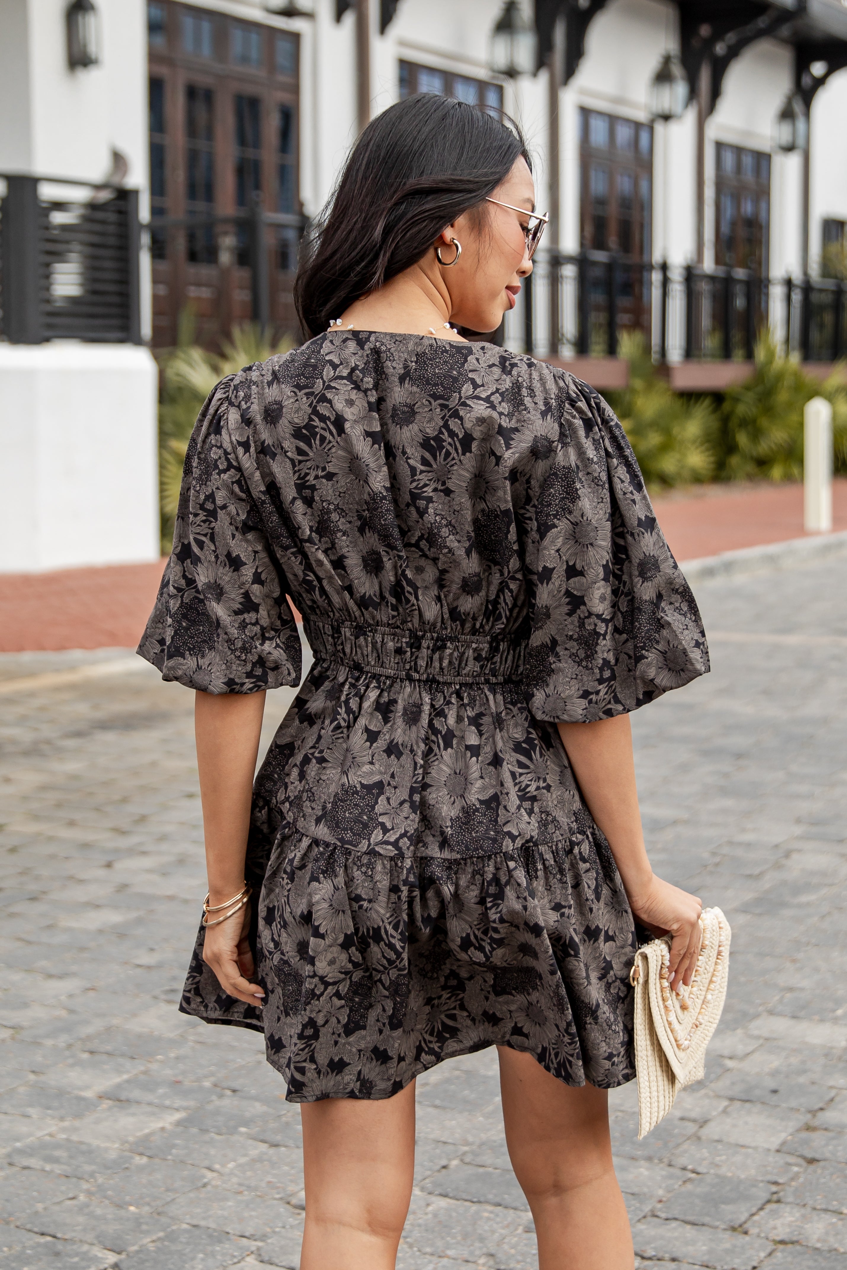 Woman wearing a black floral dress walking on a street.