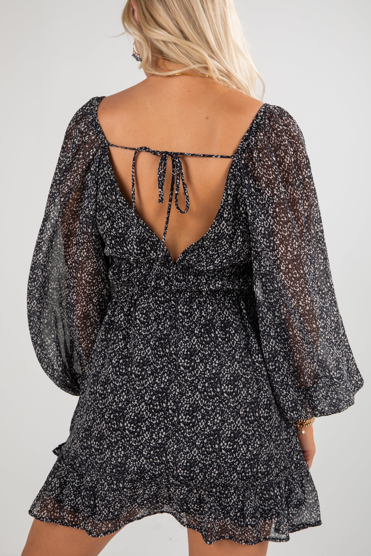 Black floral dress with sheer sleeves and open back on a plain background