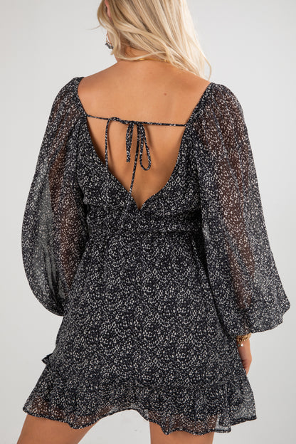 Black floral dress with sheer sleeves and open back on a plain background