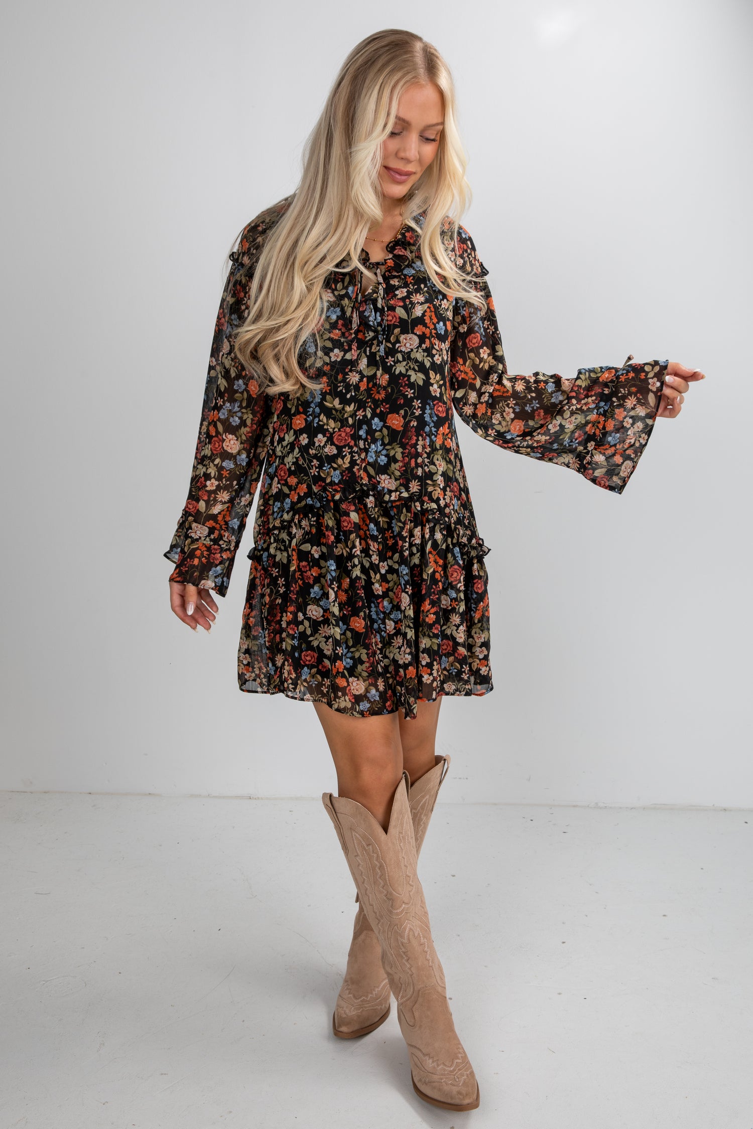 Woman wearing a floral dress with bell sleeves and beige knee-high boots on a white background