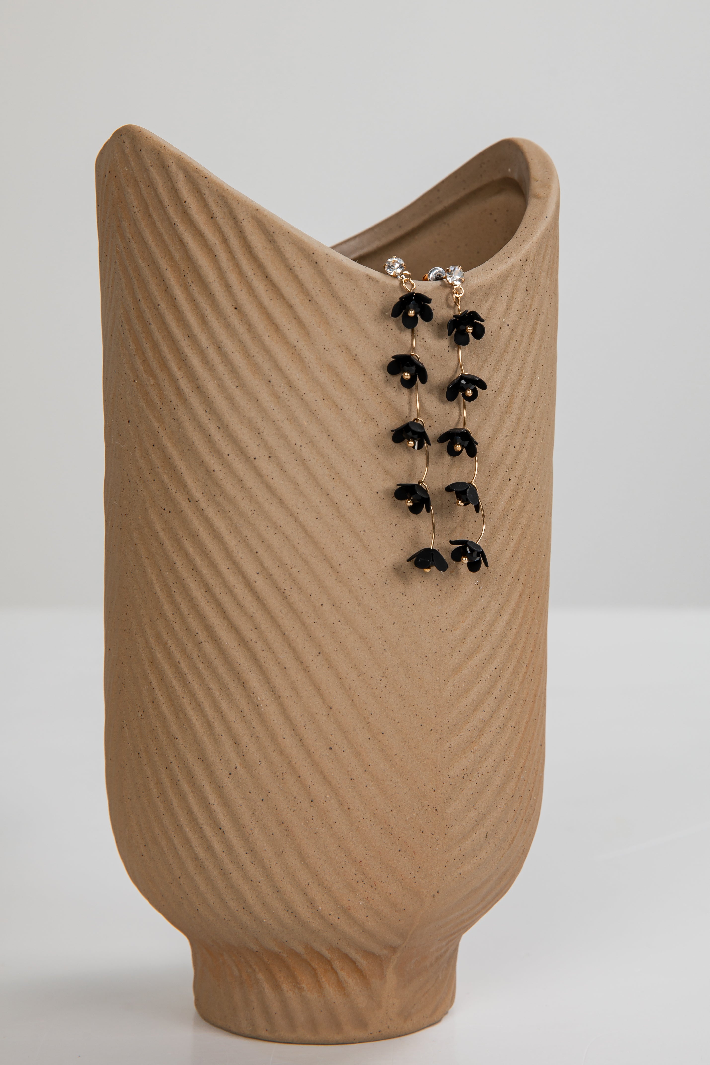 Brown textured vase with a pair of black earrings on a white background