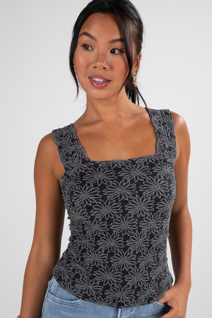Woman wearing a black floral patterned tank top against a white background