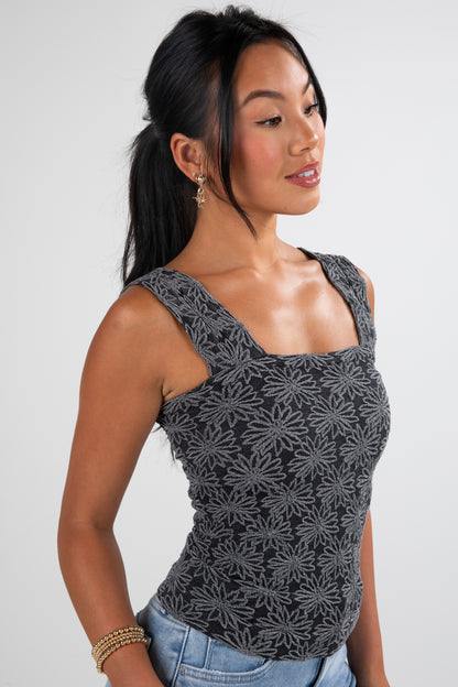 Woman wearing a black floral patterned tank top against a plain background