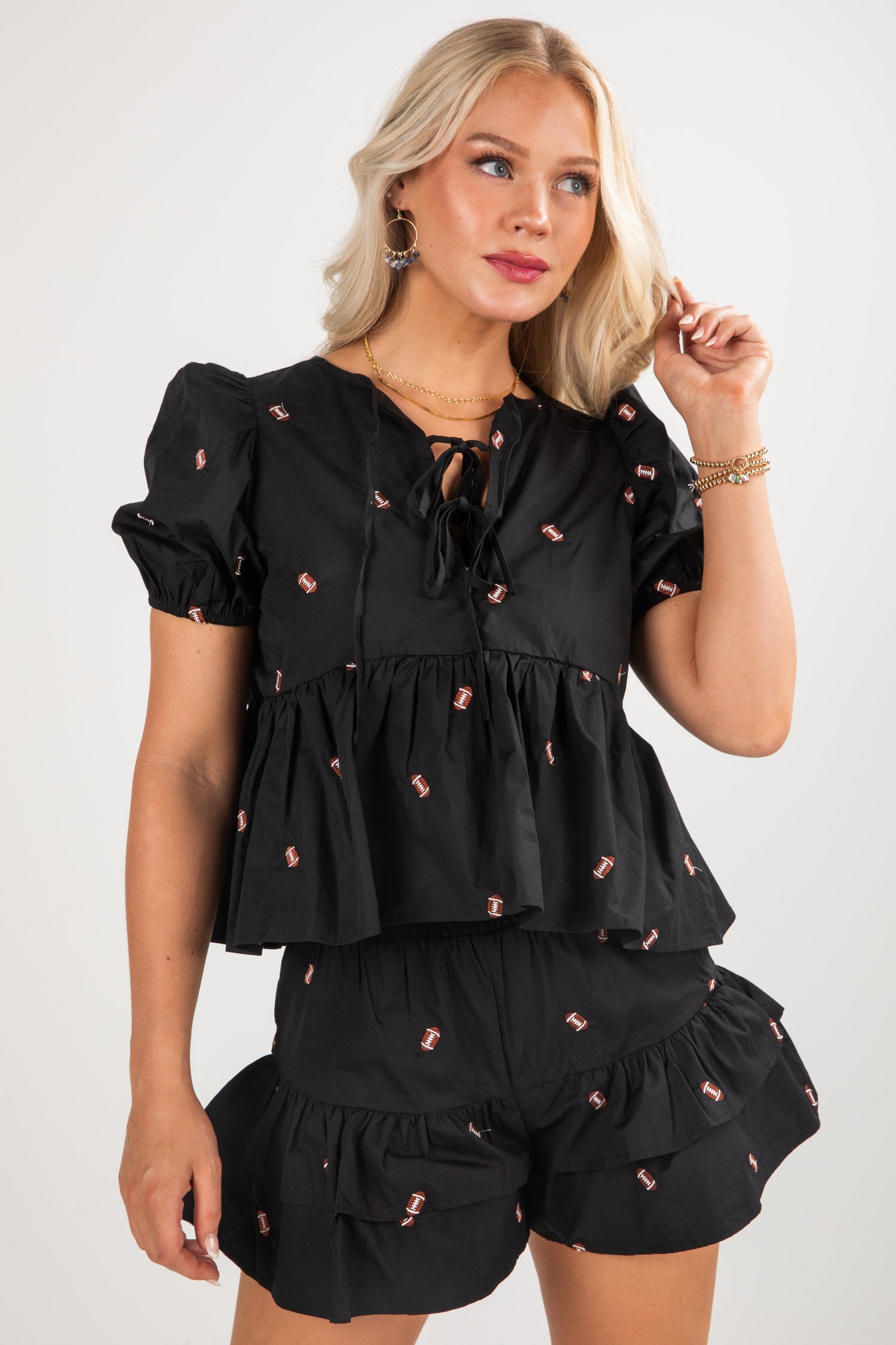 Woman wearing a black ruffled top and shorts set with pink details on a white background