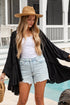 Woman in black kimono, white top, and denim shorts standing by a pool.