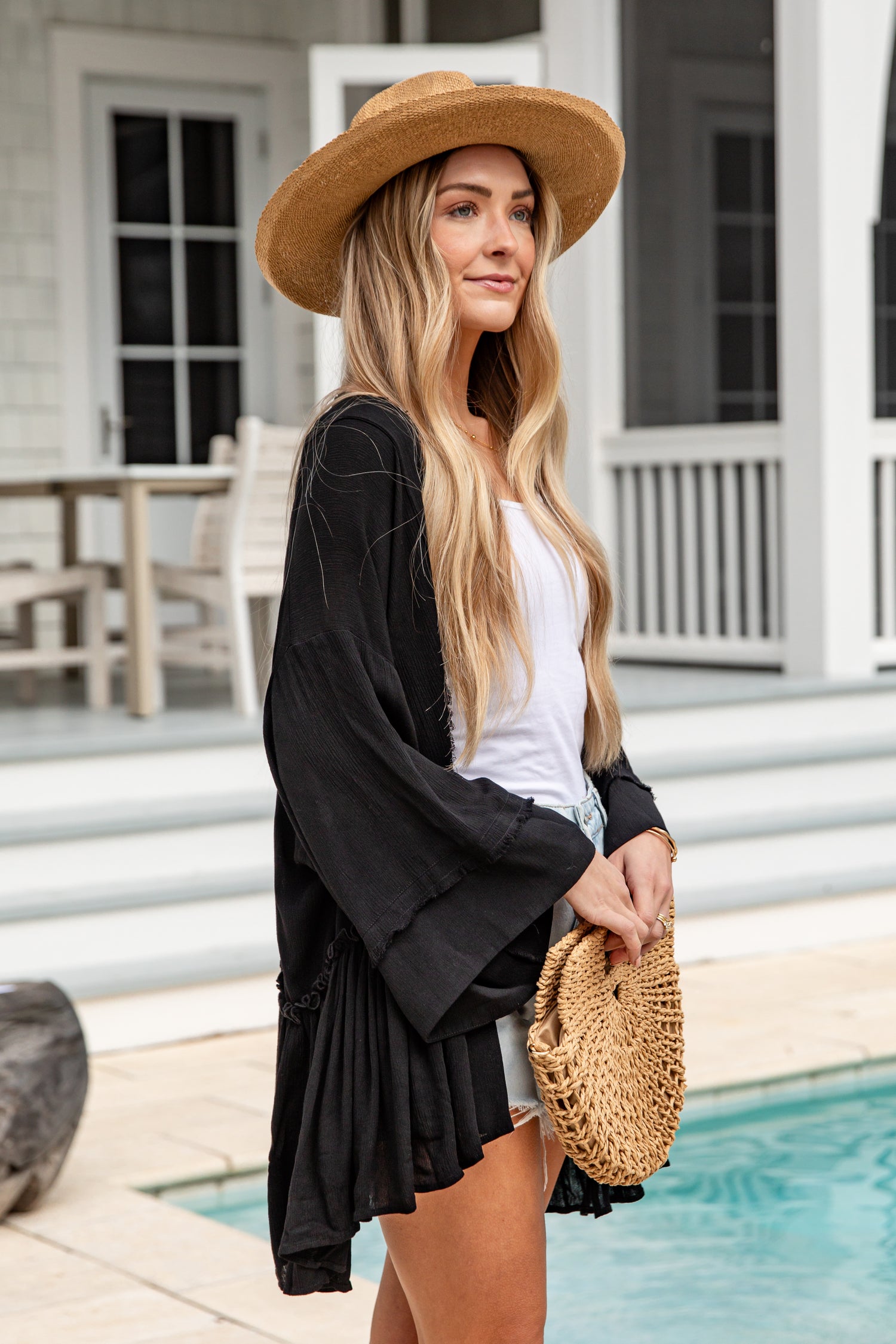 Woman in a black cardigan and straw hat by a poolside.