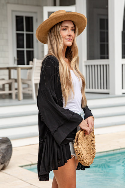 Woman in a black cardigan and straw hat by a poolside.