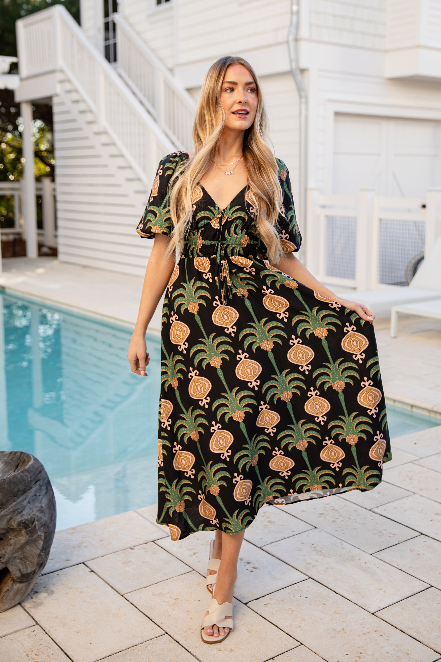 Woman in a pineapple-patterned dress standing by a pool.