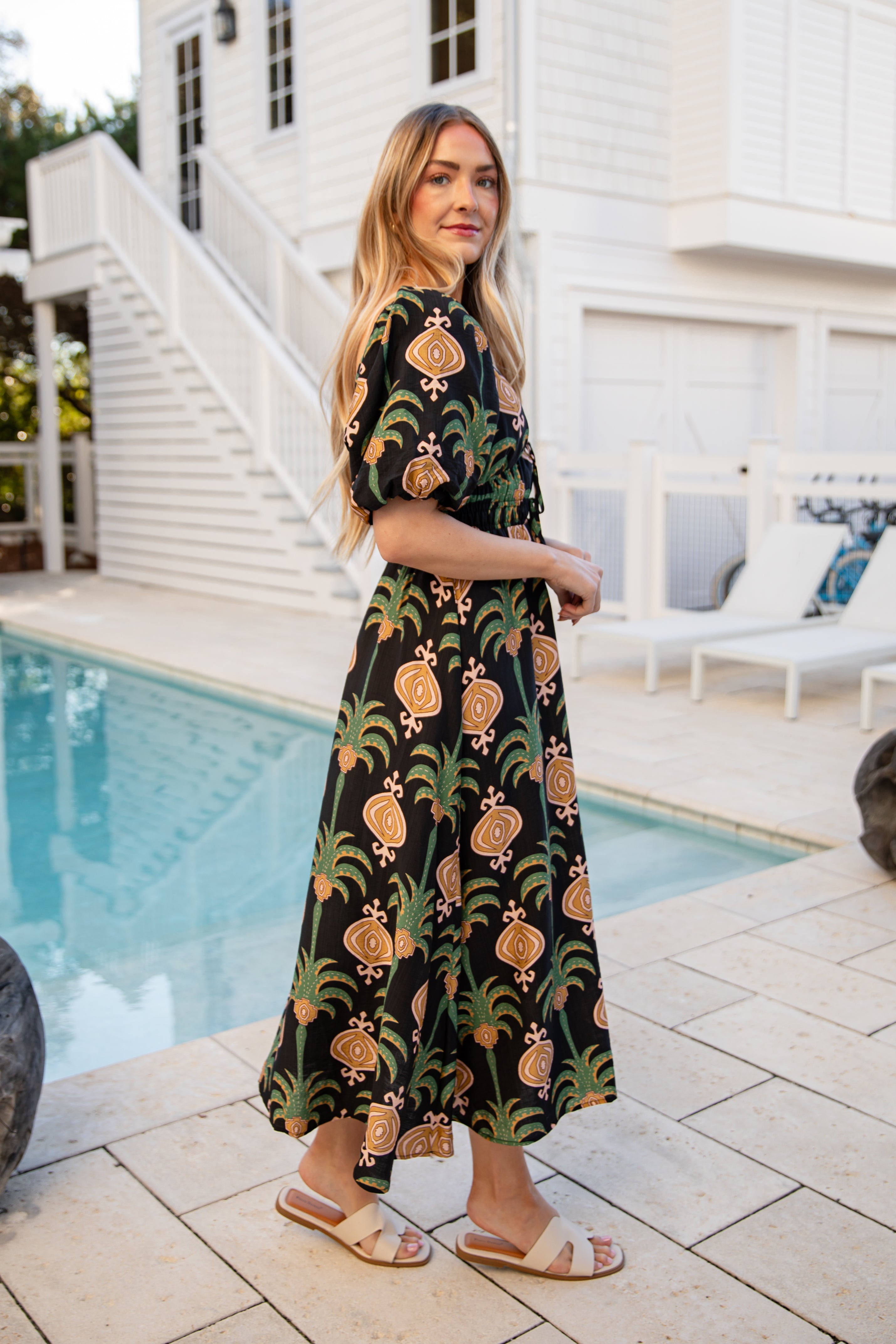 Woman in a black dress with pineapple pattern standing by a pool.