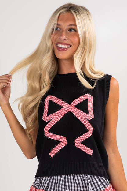 Woman wearing a black sleeveless sweater with pink bow design against a white background
