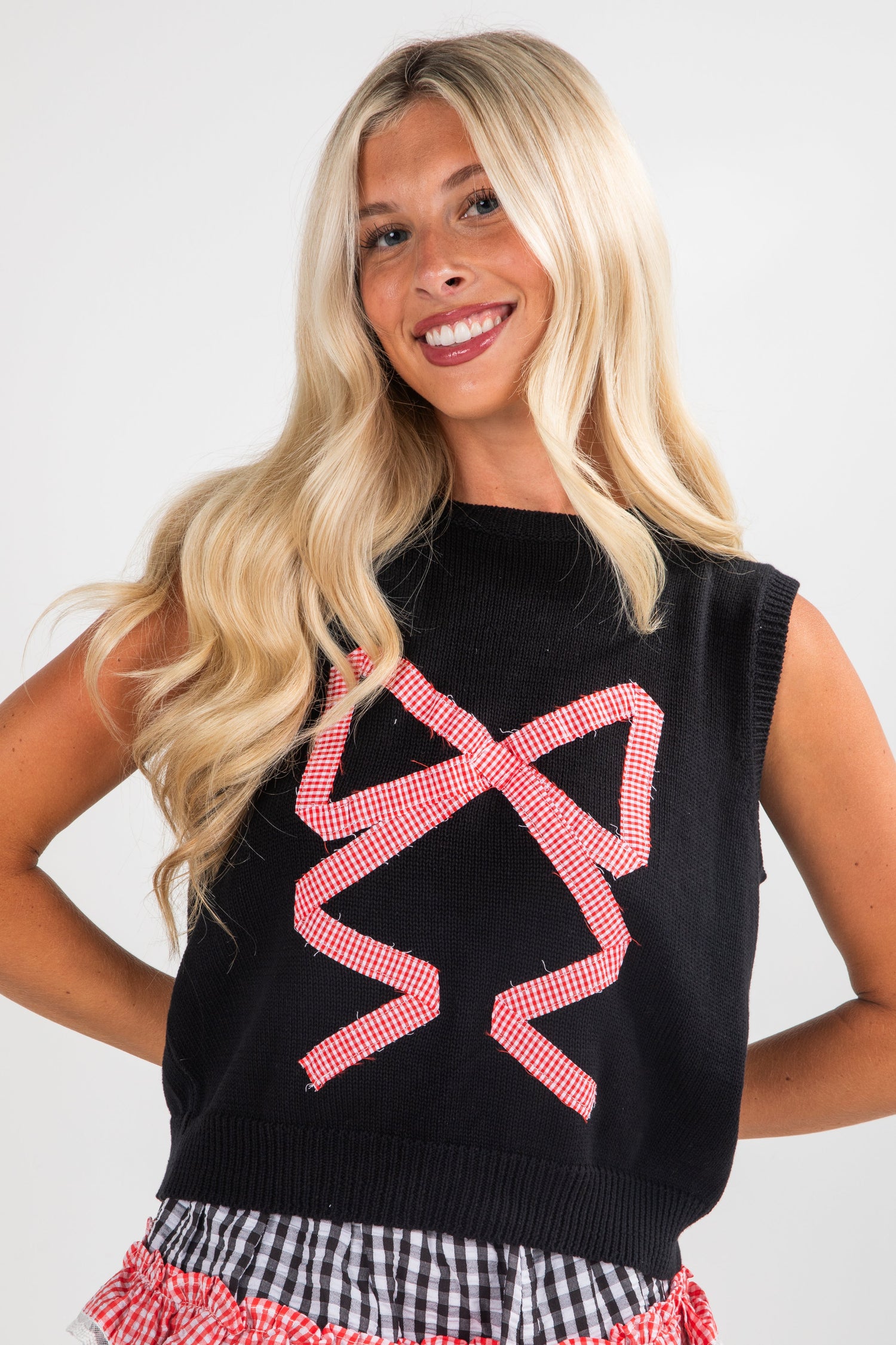 Woman wearing a black sleeveless sweater with pink geometric patterns on a white background