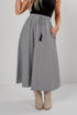 A woman wearing a high-waisted, A-line midi skirt with a black and white micro-pattern, a black top, and beige cowboy boots, standing against a light gray studio background.