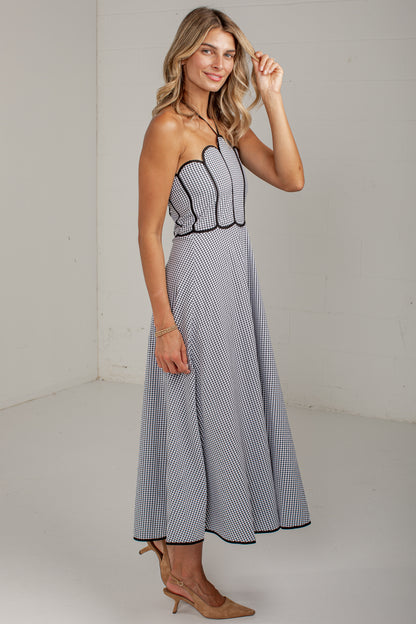 A woman modeling a strapless midi dress with a black and white gingham pattern, featuring a scalloped sweetheart bodice and a flared skirt, set against a plain white studio background.