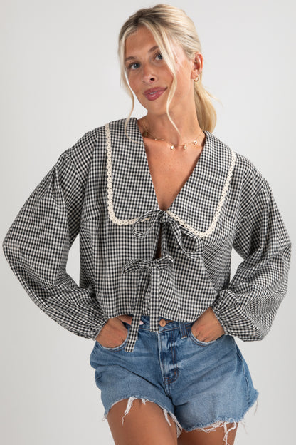 Woman wearing a checkered blouse with lace trim and denim shorts on a plain background