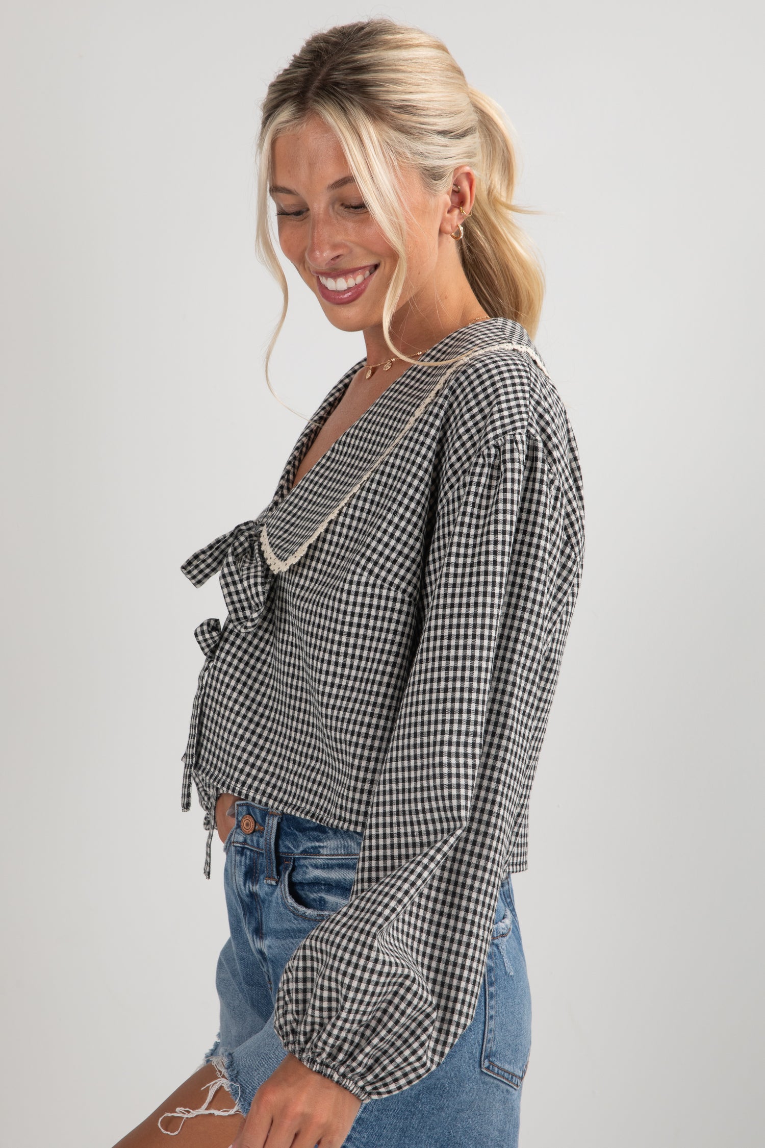 Woman wearing a black and white checkered blouse with denim shorts on a plain background