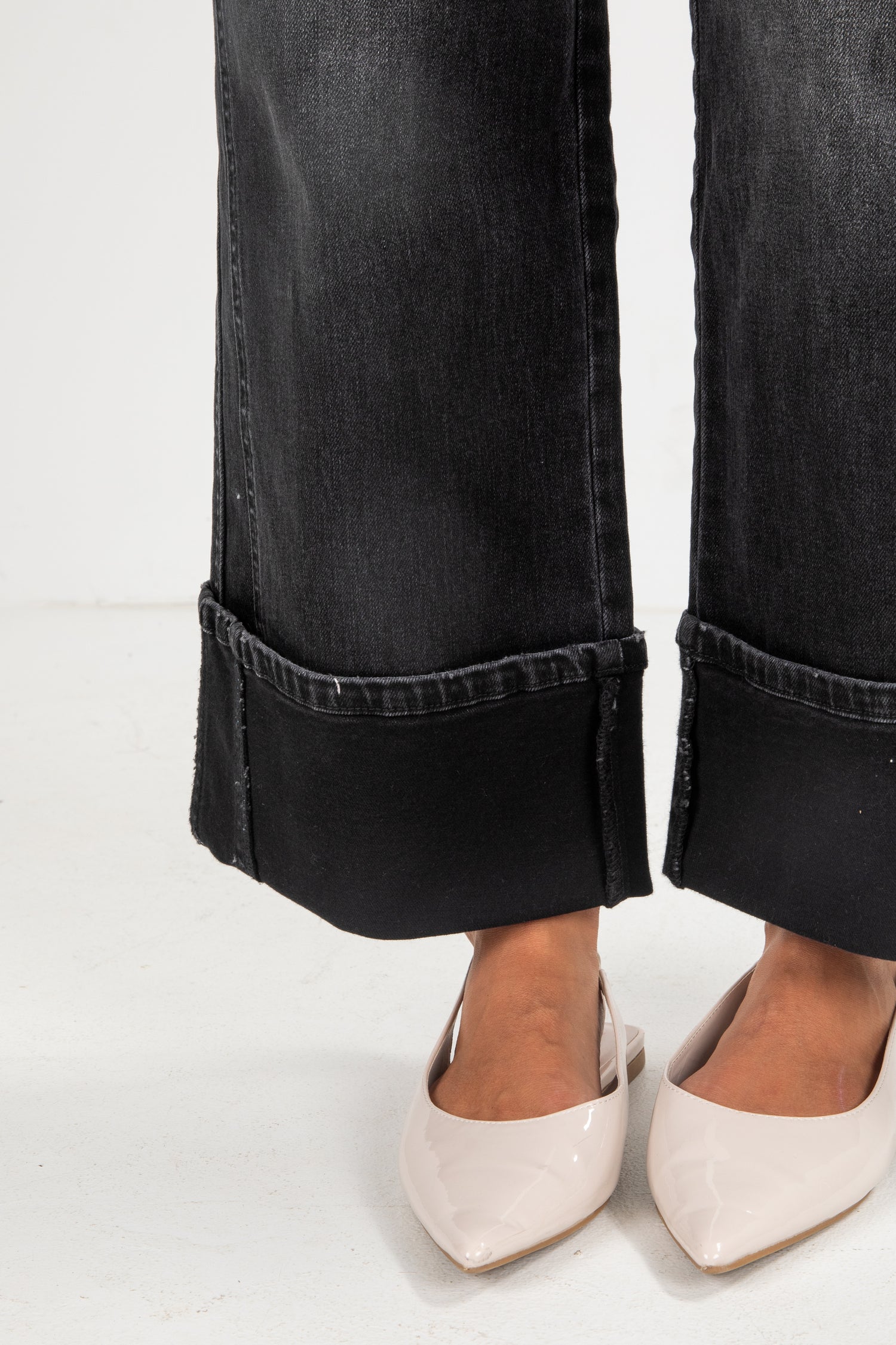 Black jeans with rolled cuffs worn by a person on a white background