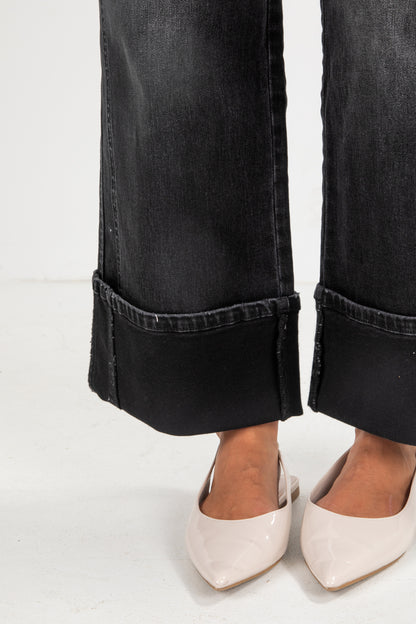 Black jeans with rolled cuffs worn by a person on a white background