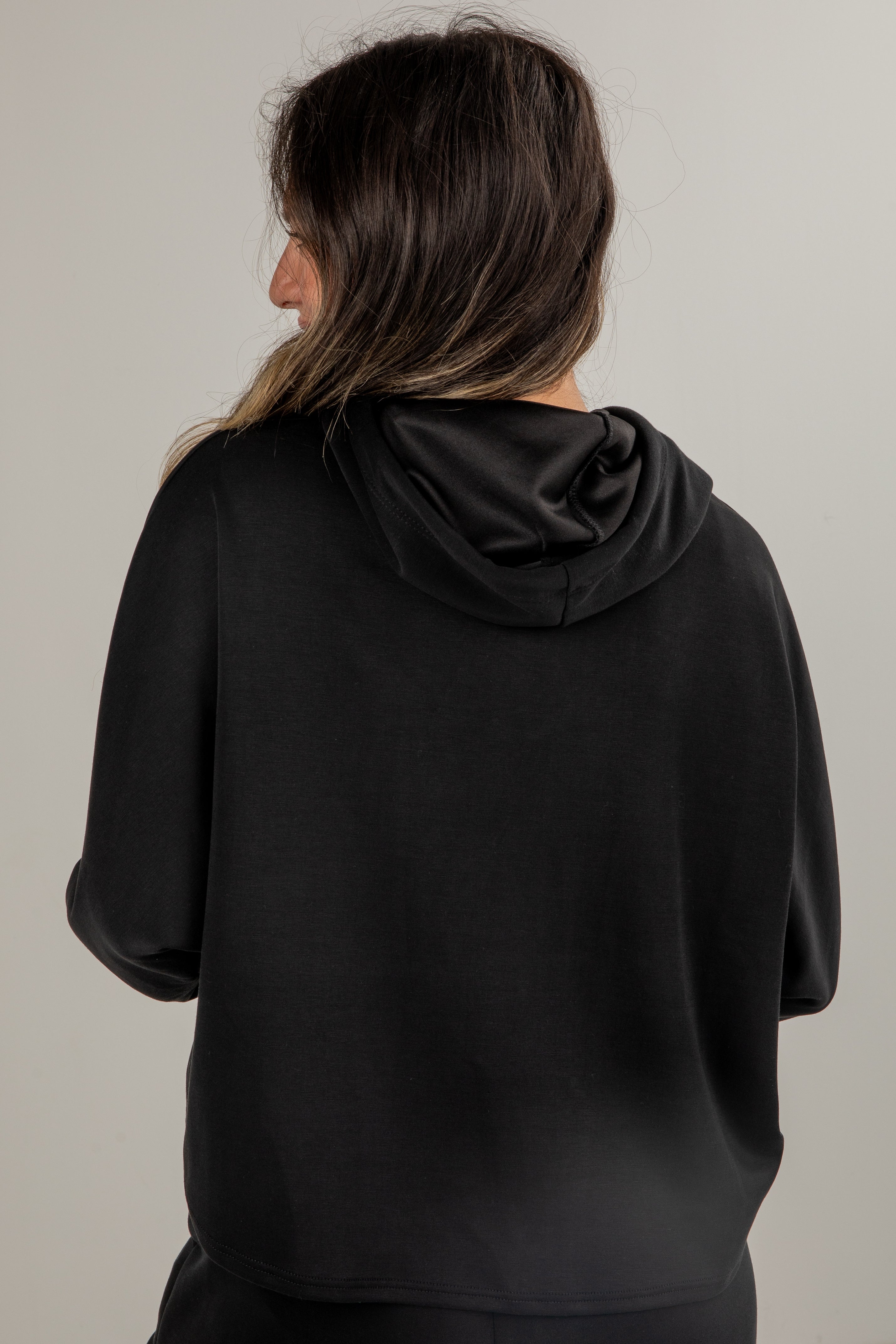 Person wearing a black hoodie from behind on a plain background