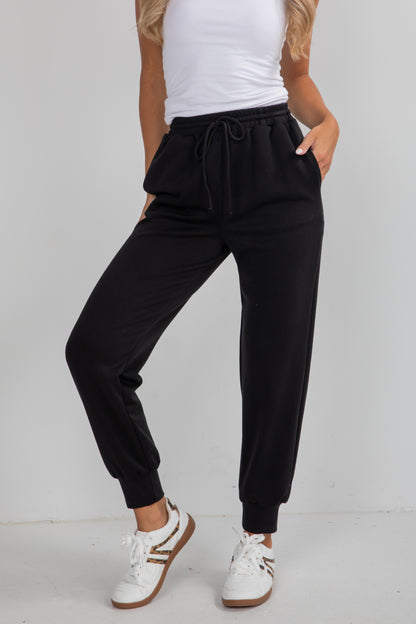 Person wearing black jogger pants and white sneakers on a plain background