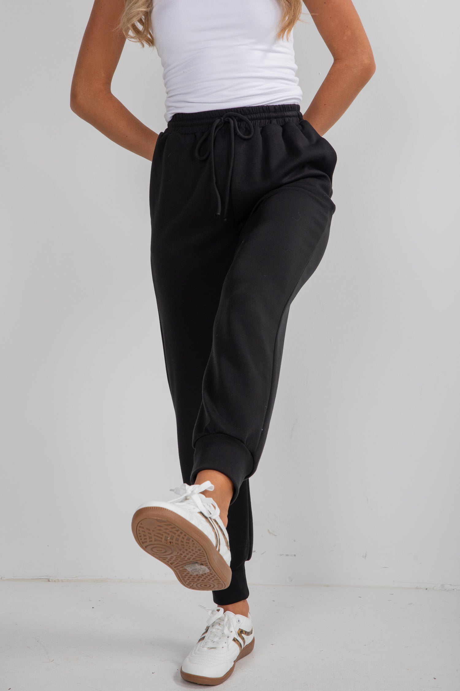 Person wearing black jogger pants and white sneakers on a plain background