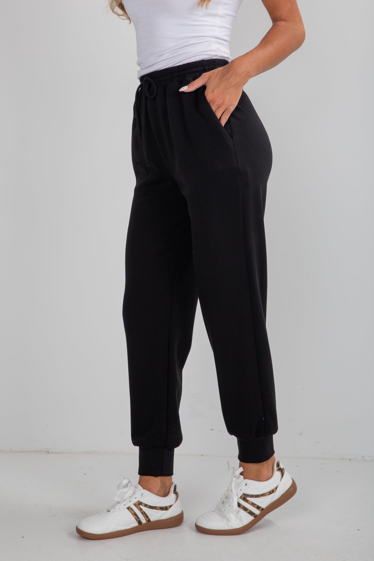 Person wearing black jogger pants and white sneakers on a plain background